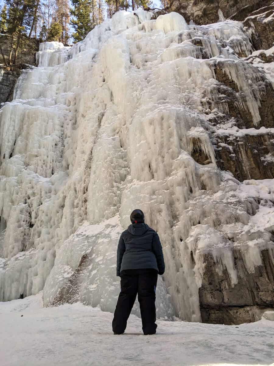 Melissa looking up at frozen waterfalls in Maligne Canyon in Jasper National Park, Canada. When the waterfalls freeze over, they turn into icicles.Some of the rock formations to the right have icicles covered. Above shows some trees and a bit of blue skies