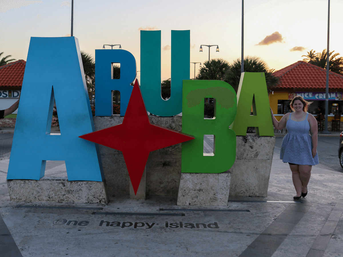 woman standing beside the aruba one happy island sign at sunset