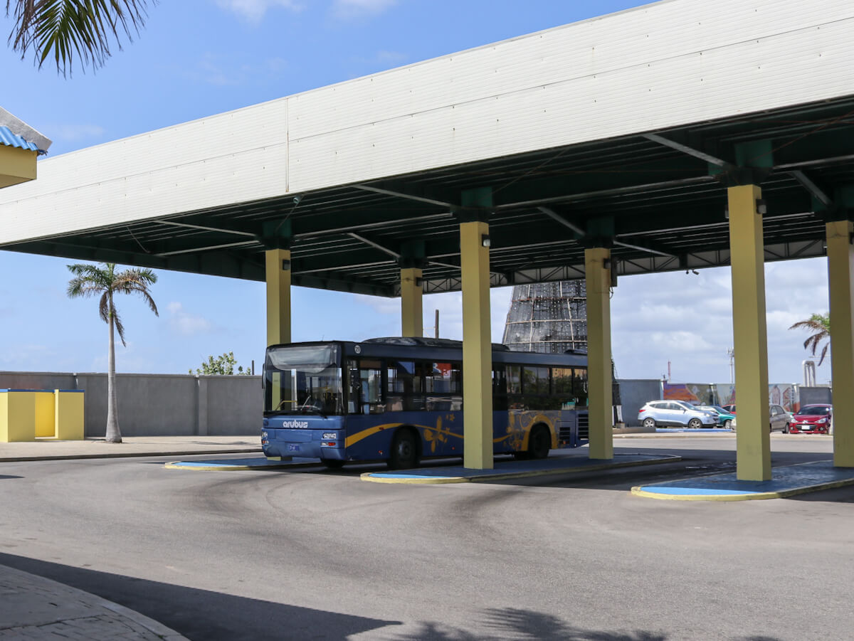 a blue and yellow bus in a bus station ready to go around aruba